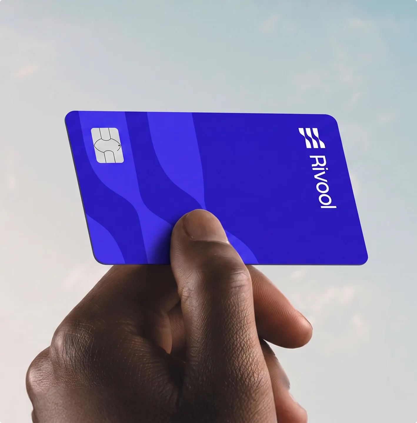 Close-up of a hand holding a blue Rivool credit card with a chip, against a light sky background.