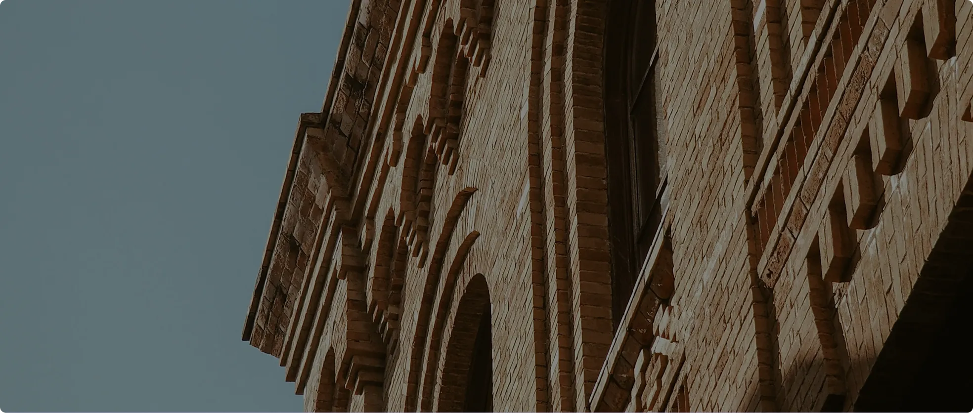 Close-up angled view of a brick building facade with multiple arched windows and detailed brickwork under a clear sky.