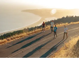 Four people walking on a paved trail at sunset on a hill overlooking a foggy coastline and ocean.
