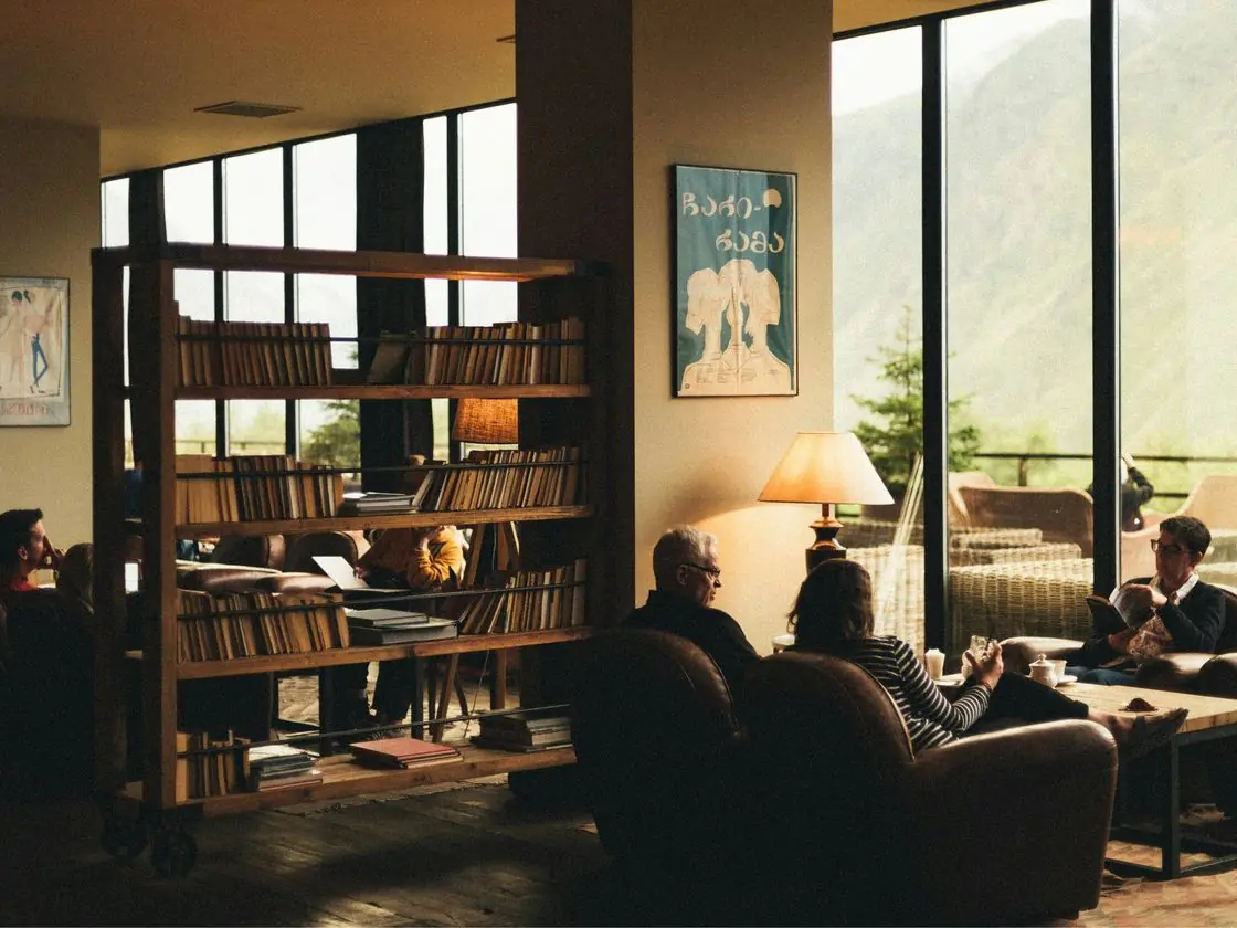 Clientes conversam num lounge com estantes de livros e janelas amplas