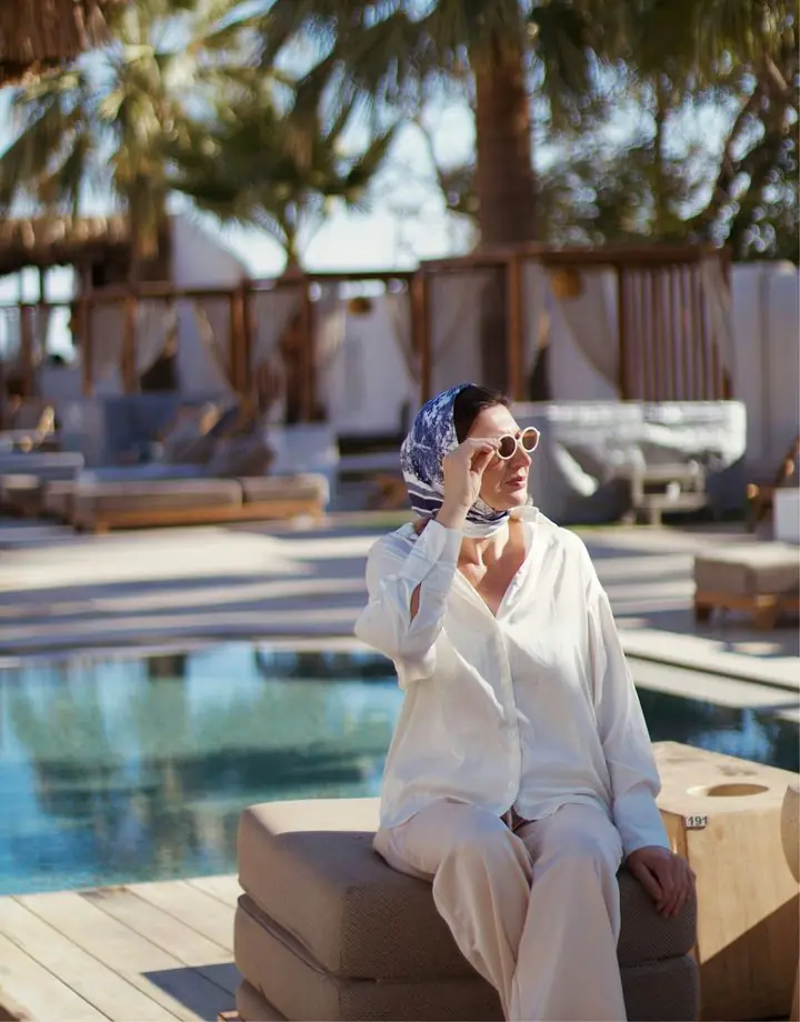 Mulher de lenço e óculos à beira da piscina de um resort