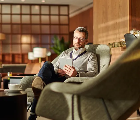 Man sitting in a lounge armchair reading on a tablet