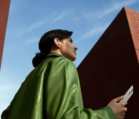 Woman in a green jacket holding her phone next to a brick building